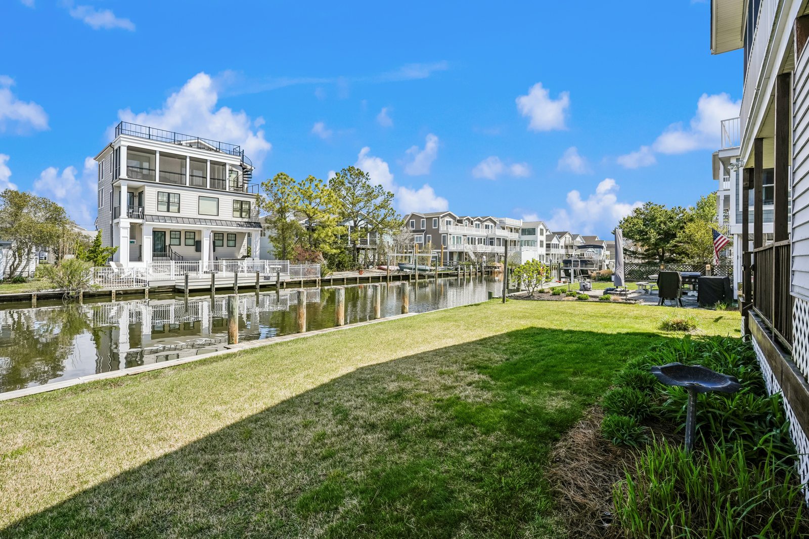 Waterfront property with grassy lawn leading to private dock access, surrounded by scenic canal views and neighboring residences under a blue sky.