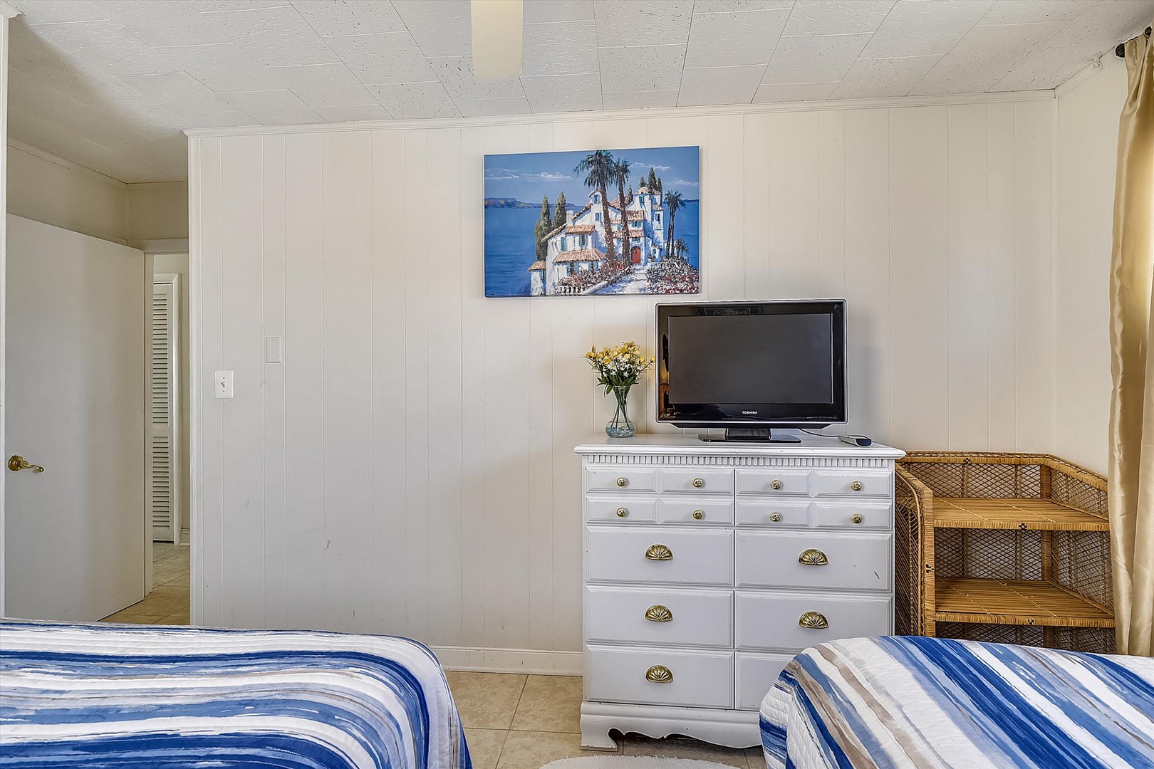 Step into your cozy retreat with comfortable twin beds, a vintage dresser topped with fresh flowers, and a TV for unwinding after exploring nearby attractions.