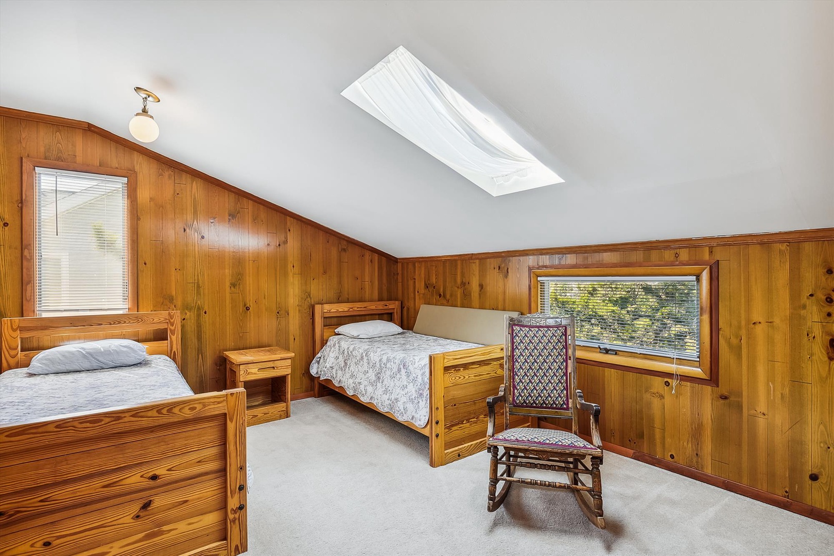 Unwind in your cozy bedroom with warm wood-paneled walls and two comfortable beds. Natural light pours in through the skylight, while a charming rocking chair invites peaceful moments.