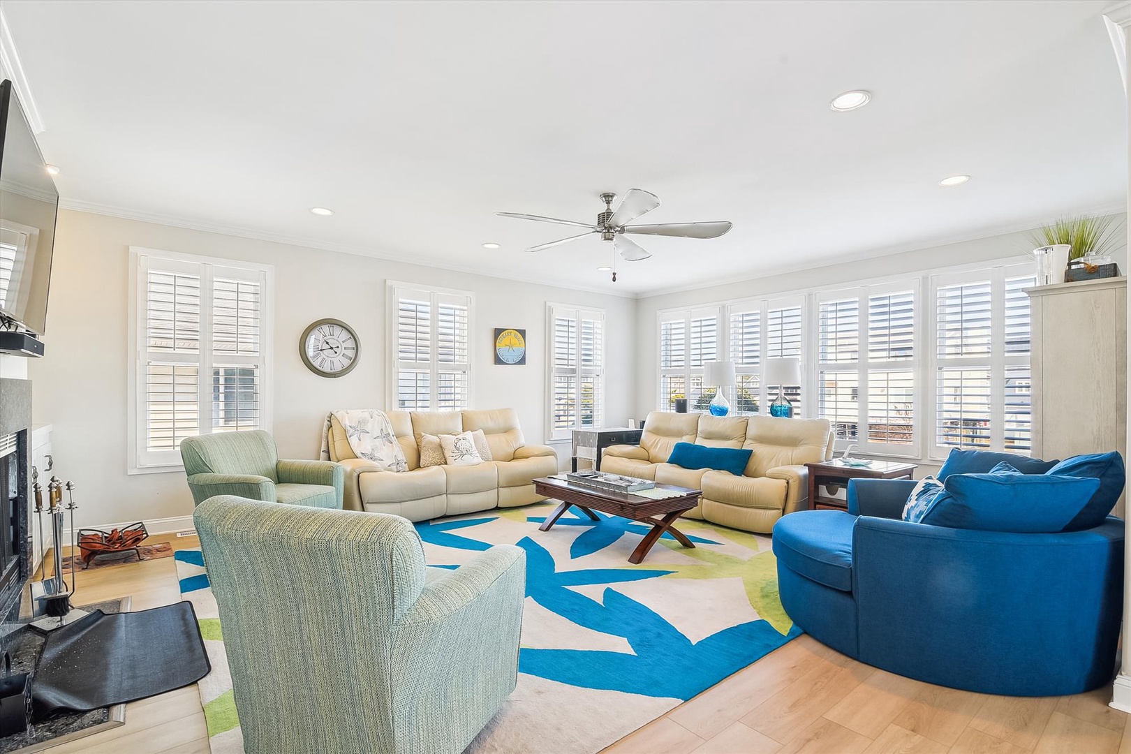 Relax in your bright living room featuring cozy seating, a vibrant rug, and abundant natural light from plantation shutters.