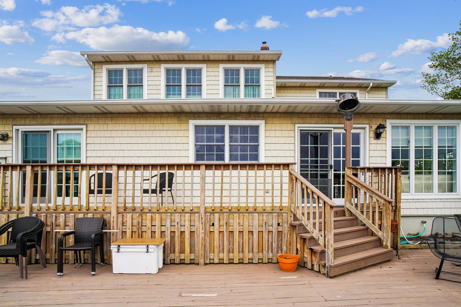 Two-story beach house with wraparound deck and spacious outdoor entertaining area featuring multiple seating zones and direct property access.