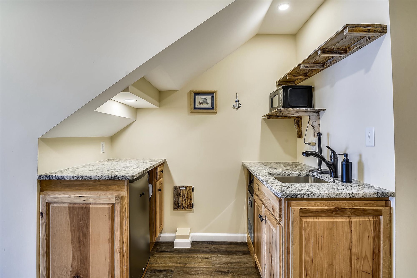 Your cozy kitchenette features rustic wood cabinetry and granite countertops, plus a convenient microwave—perfect for light meals and morning coffee in your charming attic retreat.