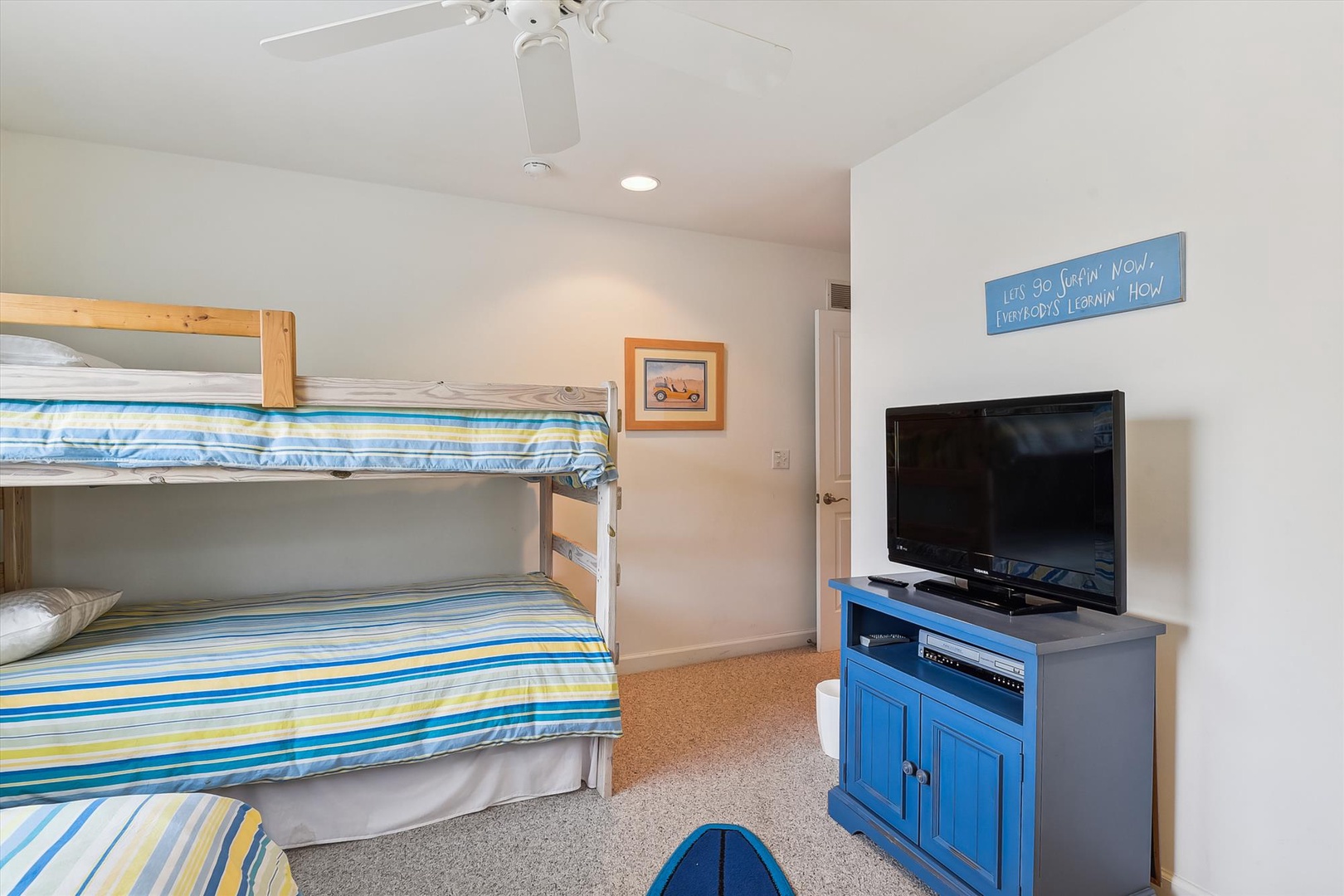 A cheerful coastal-themed bedroom features bunk beds dressed in ocean-blue striped linens, an entertainment center, and a ceiling fan to keep you comfortable. Perfect for families or groups sharing vacation memories.