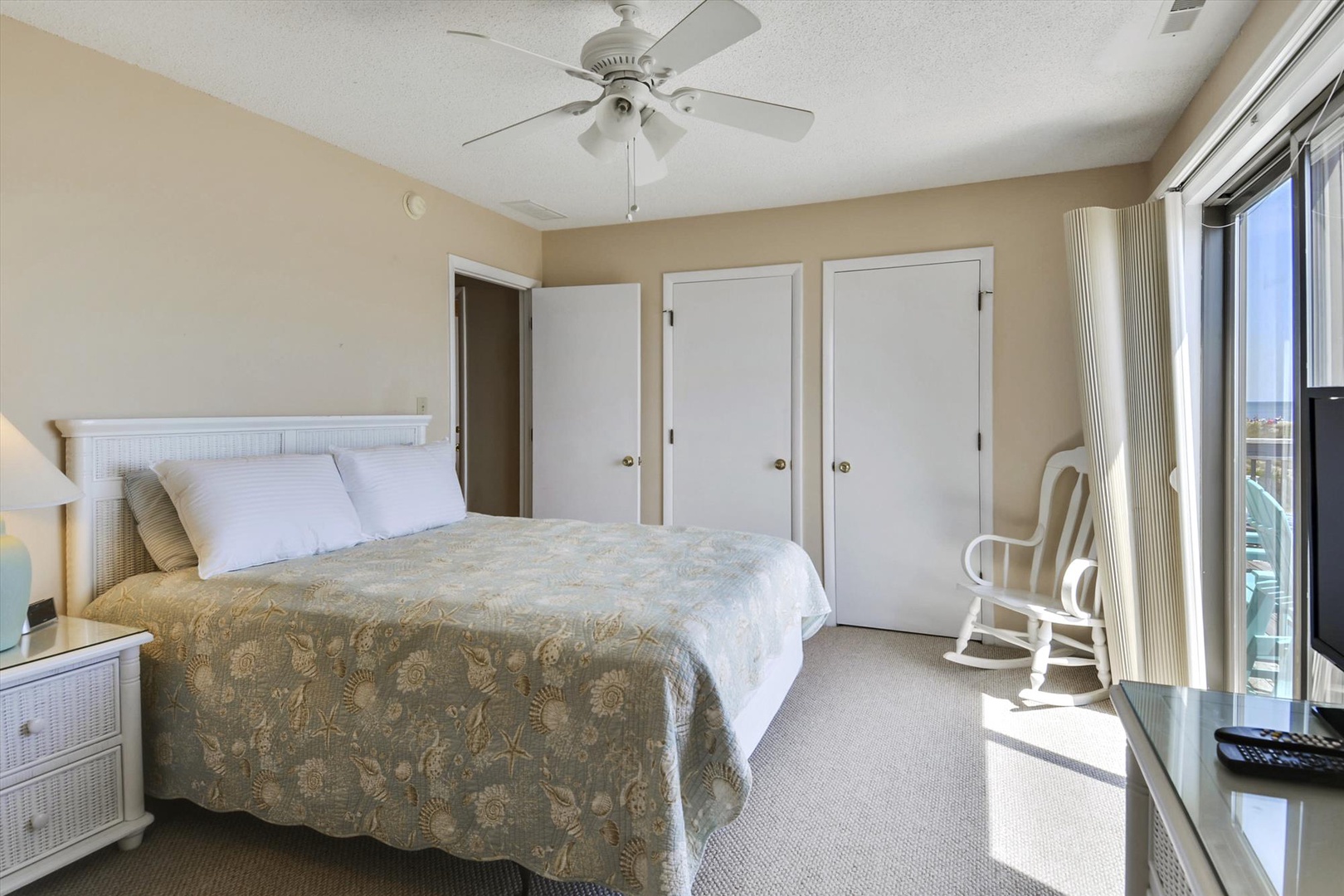 Your serene bedroom offers plush comfort with soft linens, a gentle ceiling fan, and direct access to your private balcony for relaxing moments by the ocean.