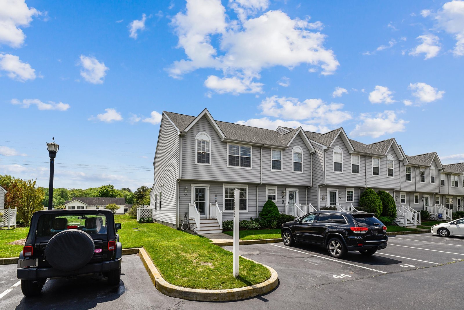 Gray-sided townhome complex with well-maintained landscaping and dedicated parking spaces in a quiet residential setting.