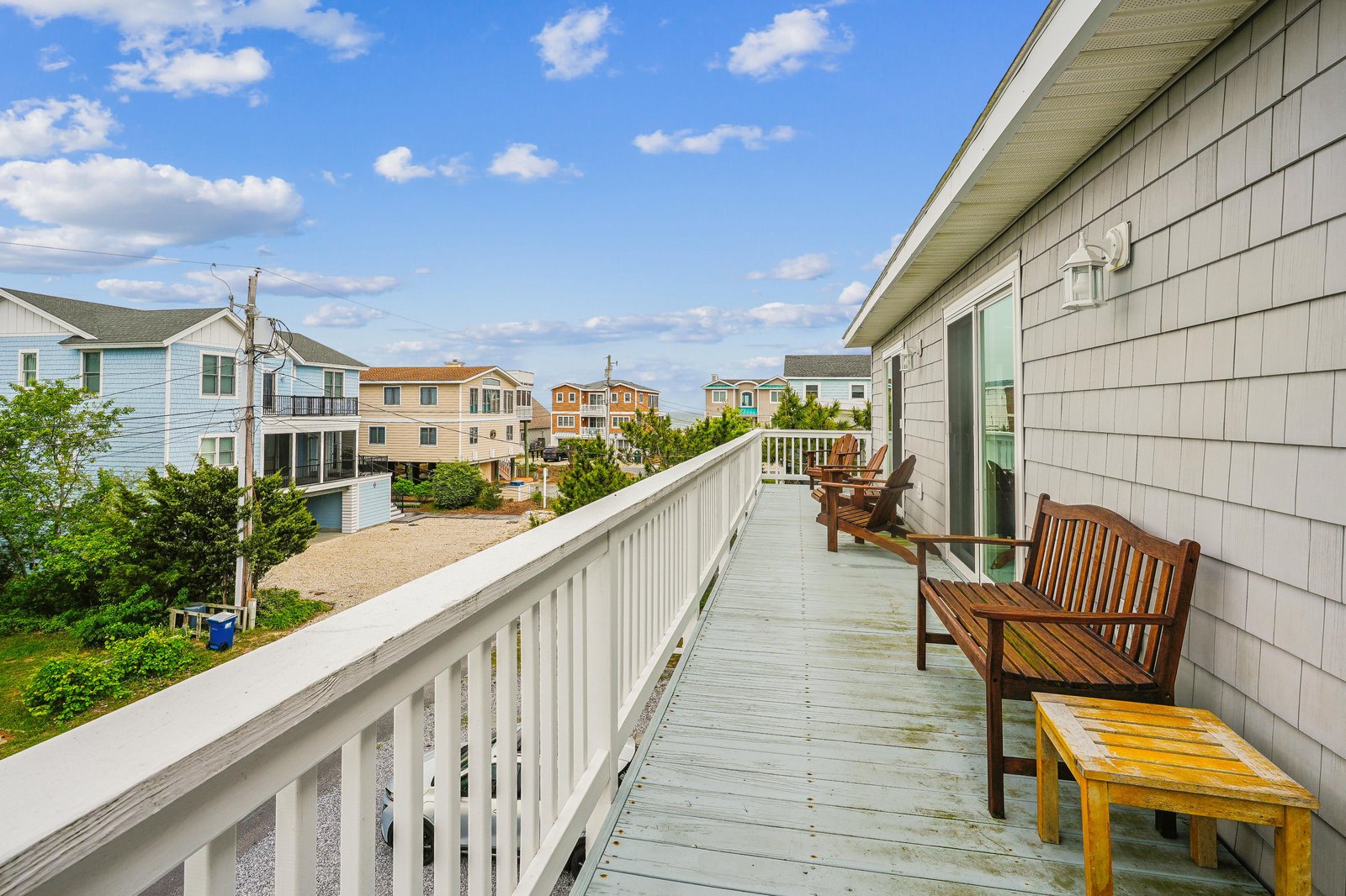 A spacious balcony with comfortable wooden seating overlooks a peaceful residential neighborhood, inviting you to unwind with your morning coffee or evening sunset views.