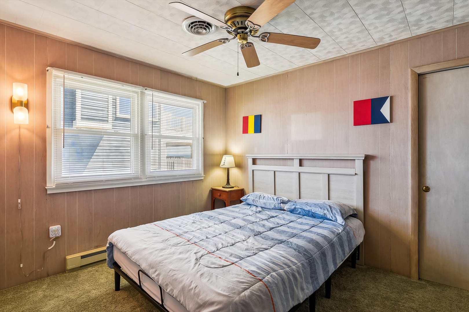 Settle into your cozy bedroom featuring a comfy bed, ceiling fan, and natural light from large windows. Nautical touches add coastal charm to your restful retreat.