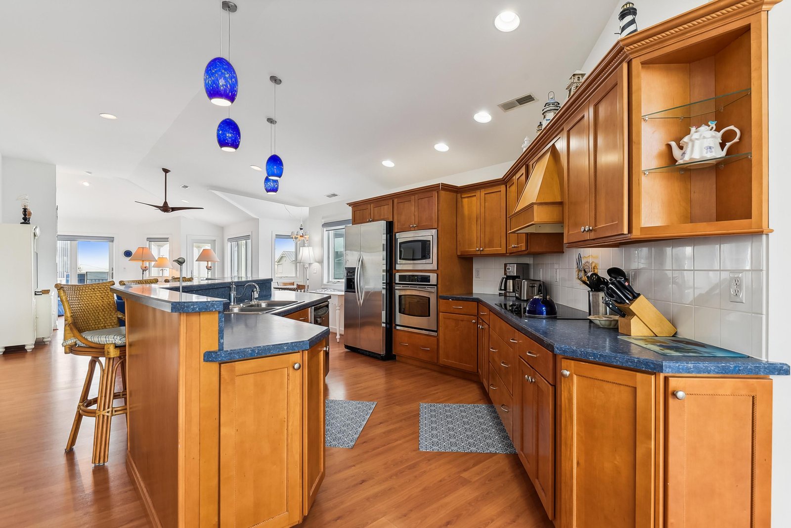 Step into your fully equipped gourmet kitchen, where warm wood cabinetry and gleaming countertops set the stage for home-cooked meals. Blue pendant lighting adds a coastal touch, while the island invites you to gather, cook, and create memories.