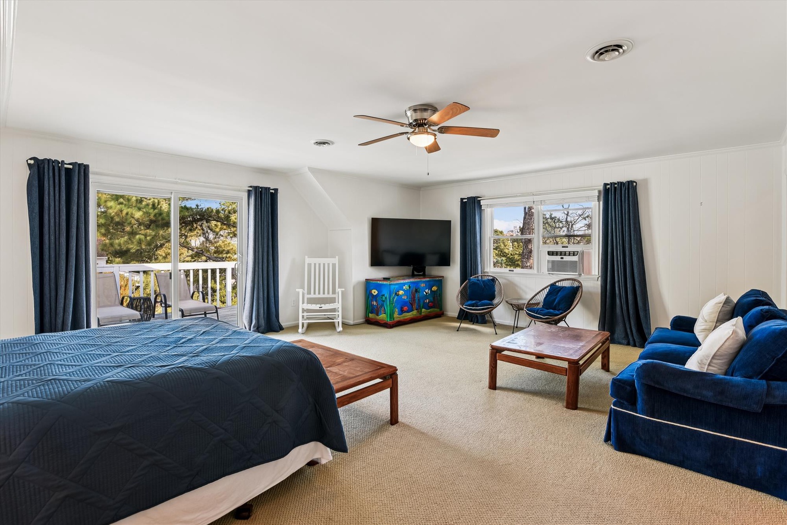 Relax in your spacious bedroom suite featuring a comfy blue sofa, ceiling fan, and peaceful balcony views through large windows.