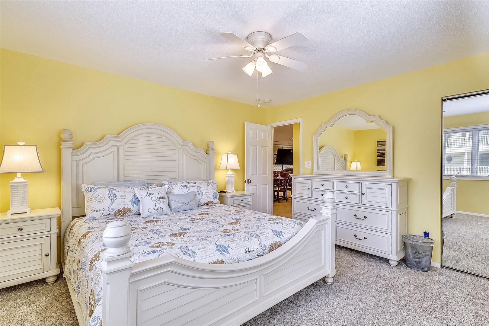 Step into your bright coastal bedroom with cheerful yellow walls, a plush queen bed, and crisp white furnishings that create your perfect beach retreat.