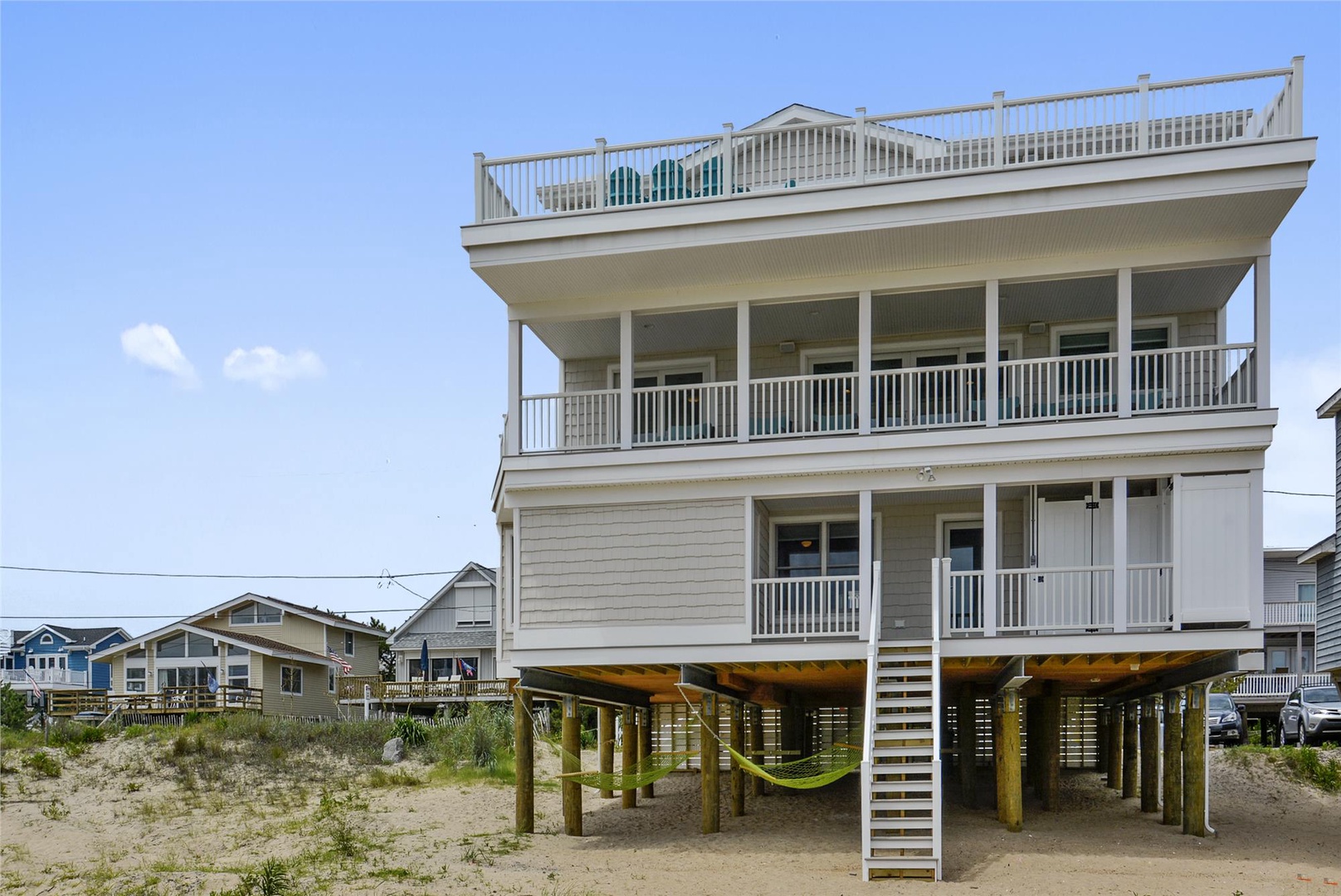 A three-story beachfront property on stilts with expansive decks, situated in a quiet coastal neighborhood with direct sandy beach access.