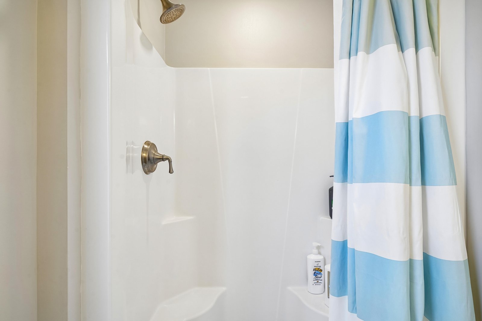 Step into your private shower with bright tile and brushed bronze fixtures, where a cheerful striped curtain adds a pop of coastal color to your refreshing morning routine.