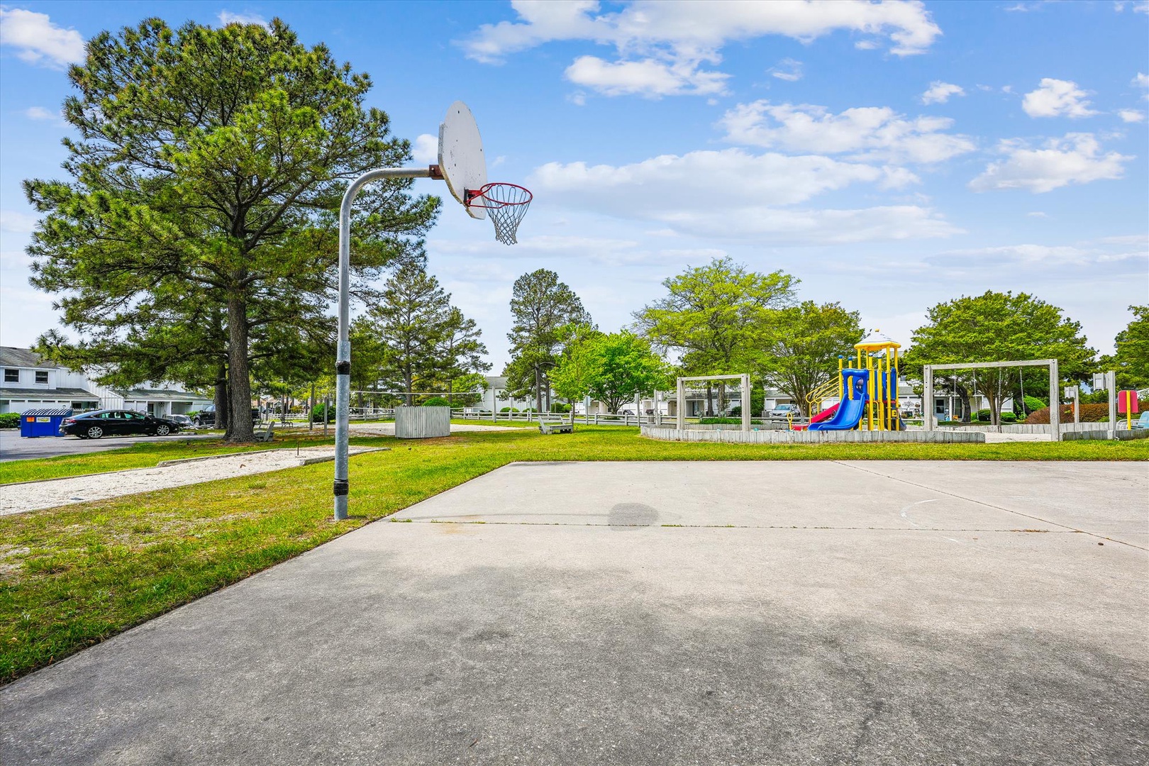 Outdoor recreational area featuring basketball court and playground equipment surrounded by mature trees and green spaces.