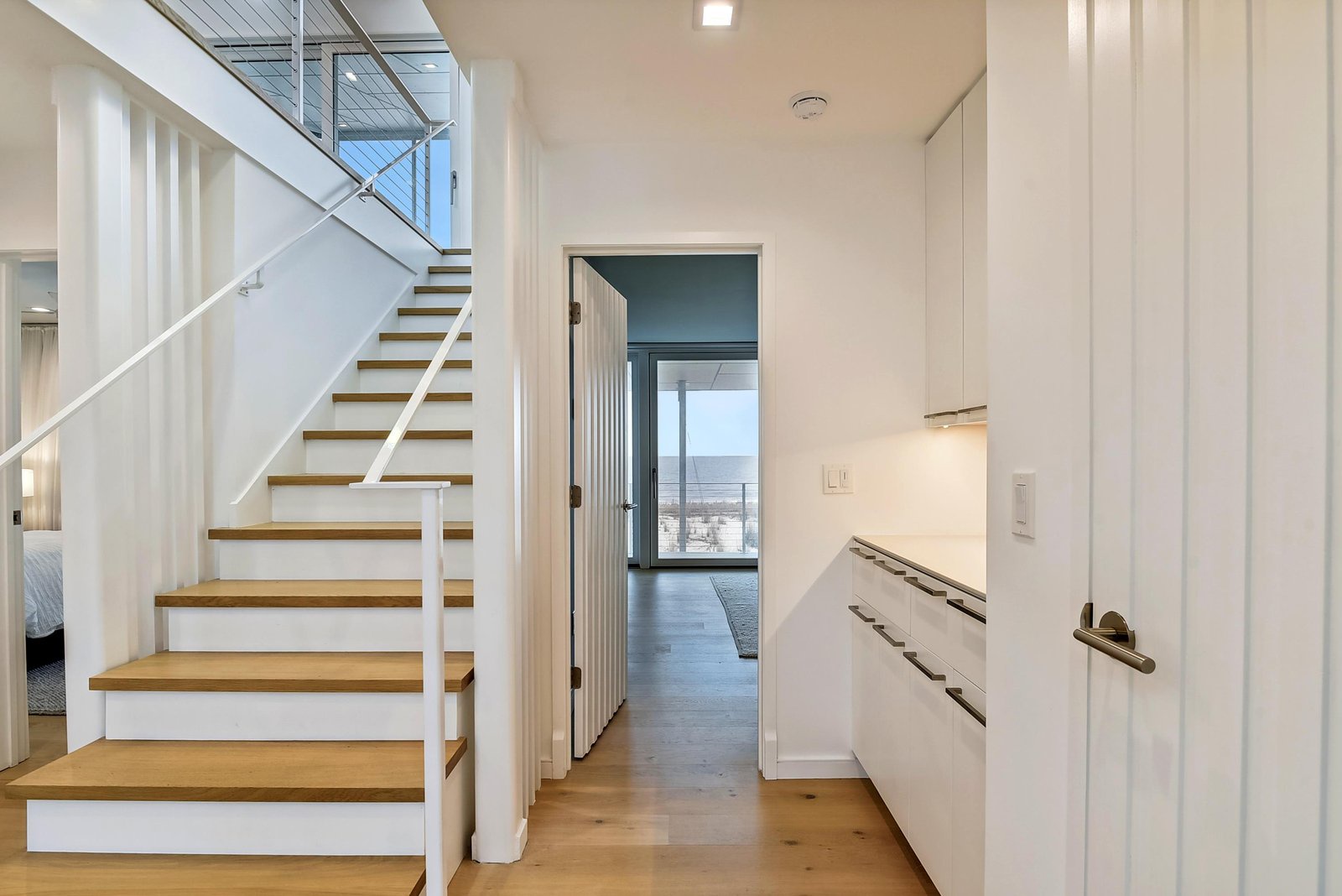 Step inside your beautifully designed retreat, where natural light and modern Scandinavian touches create an inviting first impression. The open staircase draws your eye upward, while glimpses of the sea beckon from beyond.