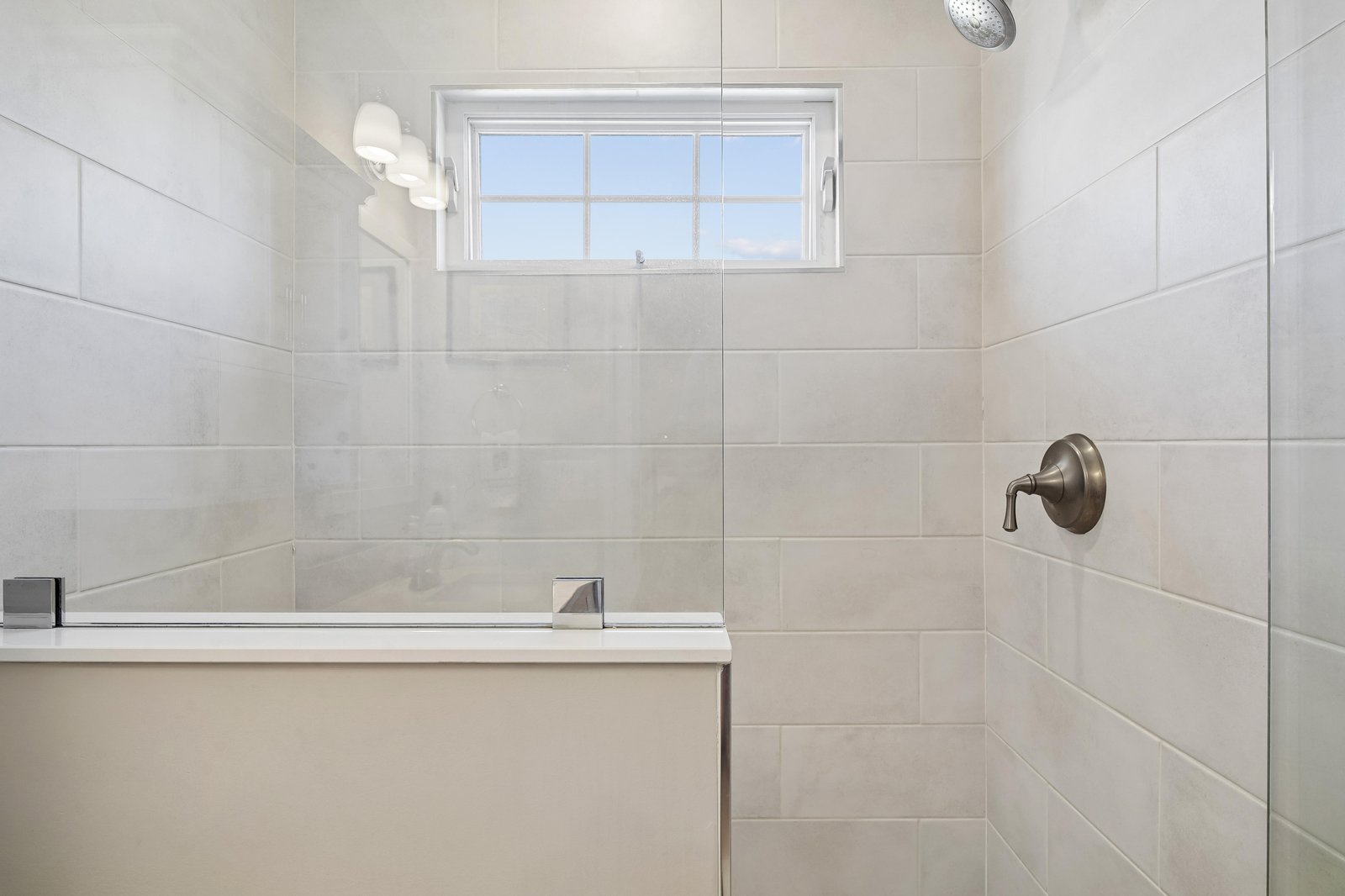 Step into your private spa-like sanctuary with elegant tile work, a spacious glass-enclosed shower, and soft natural light streaming through the window above.