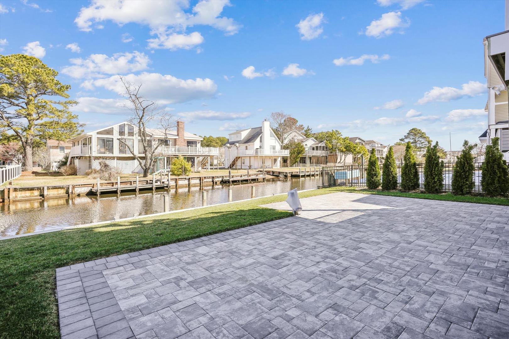 Waterfront property features private dock access and a spacious paver patio overlooking a serene canal with neighboring homes in a coastal community setting.