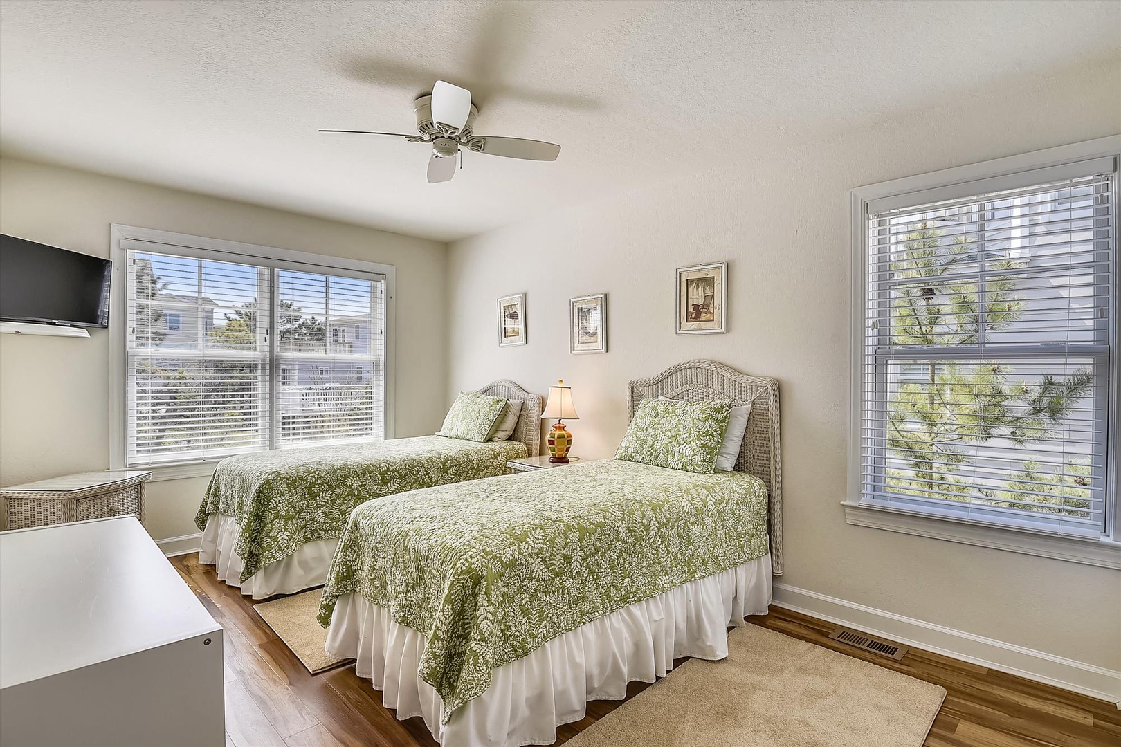 Relax in your bright twin bedroom featuring green botanical bedding, ceiling fan, and peaceful neighborhood views through large windows.