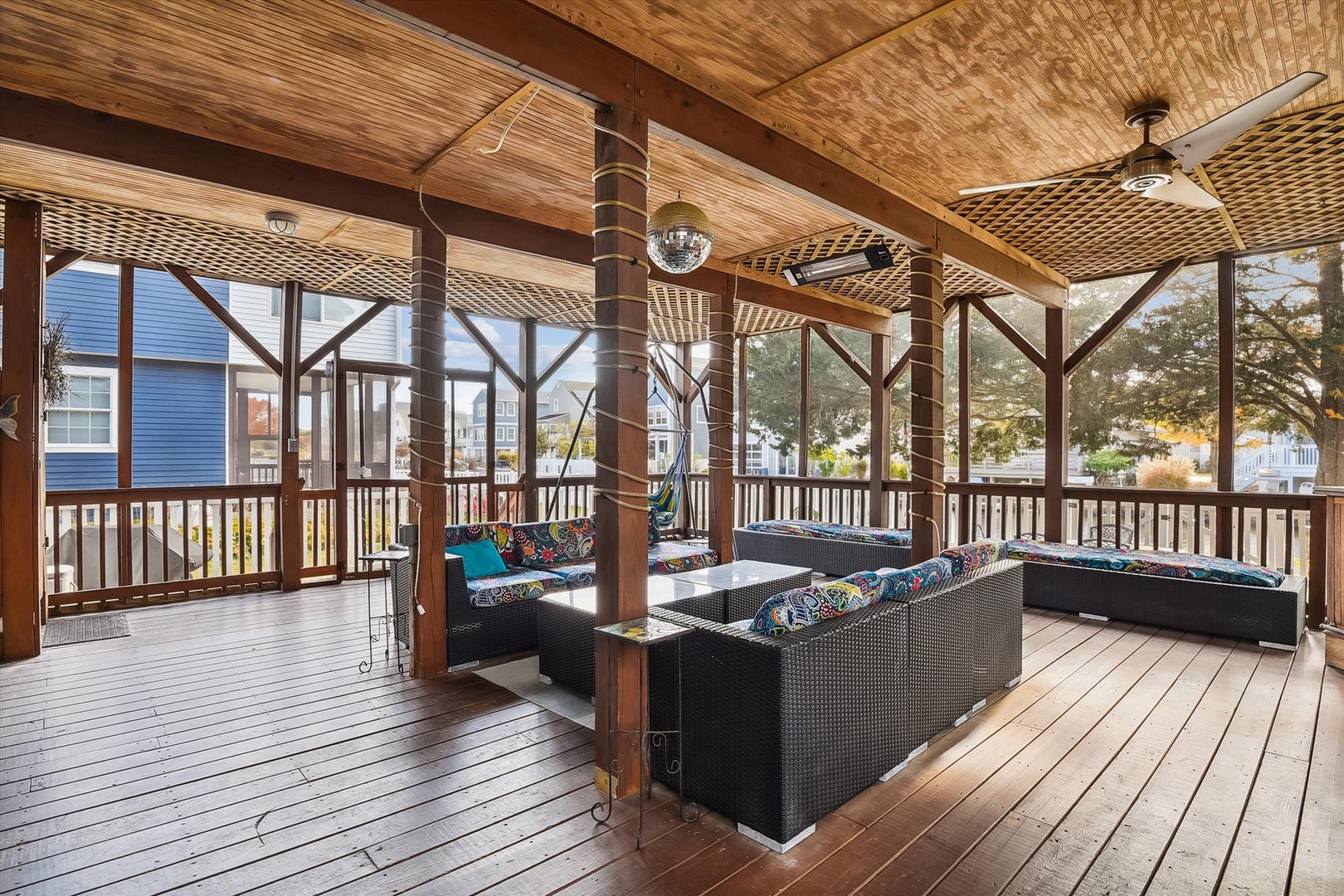 This spacious screened porch overlooks a residential neighborhood, offering a shaded outdoor retreat with ceiling fans, wicker furniture, and a disco ball accent for relaxed entertaining.