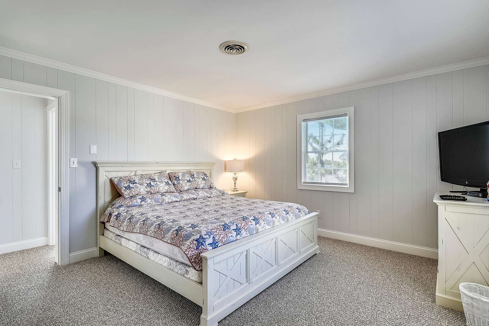 Step into your serene coastal bedroom with crisp white shiplap walls and a cozy bed dressed in nautical linens. Natural light filters through the window, creating a peaceful retreat for restful nights.