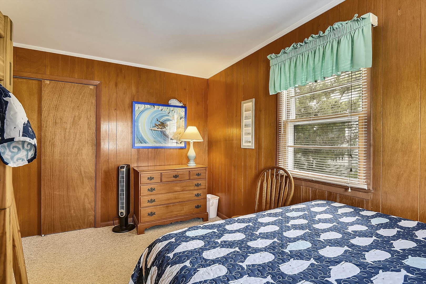 Settle into your cozy coastal bedroom with warm wood paneling, a comfy bed dressed in charming nautical linens, and natural light filtering through the window—your peaceful retreat awaits.