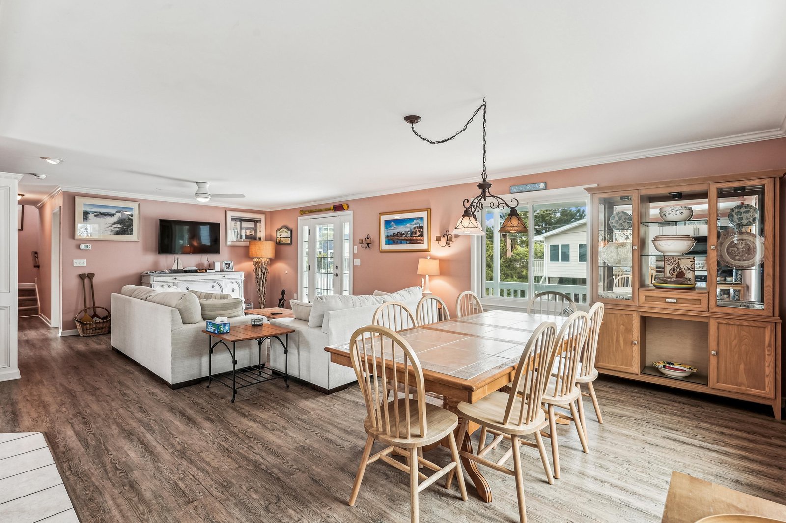 Spacious open-plan living and dining area with warm coastal charm. Farmhouse-style table, plush sectional, and French doors opening to a private deck filled with natural light.