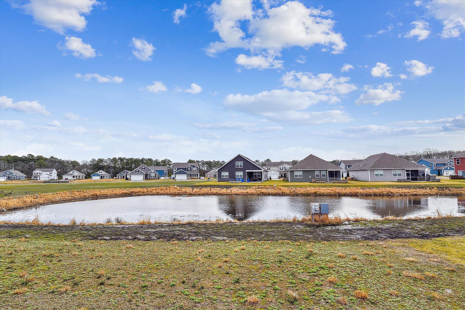 Peaceful residential community featuring a serene pond surrounded by modern homes under expansive blue skies.