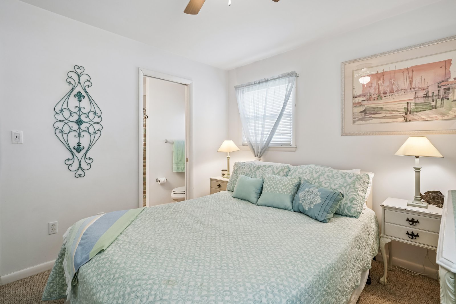 You'll love waking up in this cozy coastal bedroom, where soft seafoam linens and charming decor create a peaceful retreat. Natural light filters through sheer curtains, making your mornings bright and relaxing.