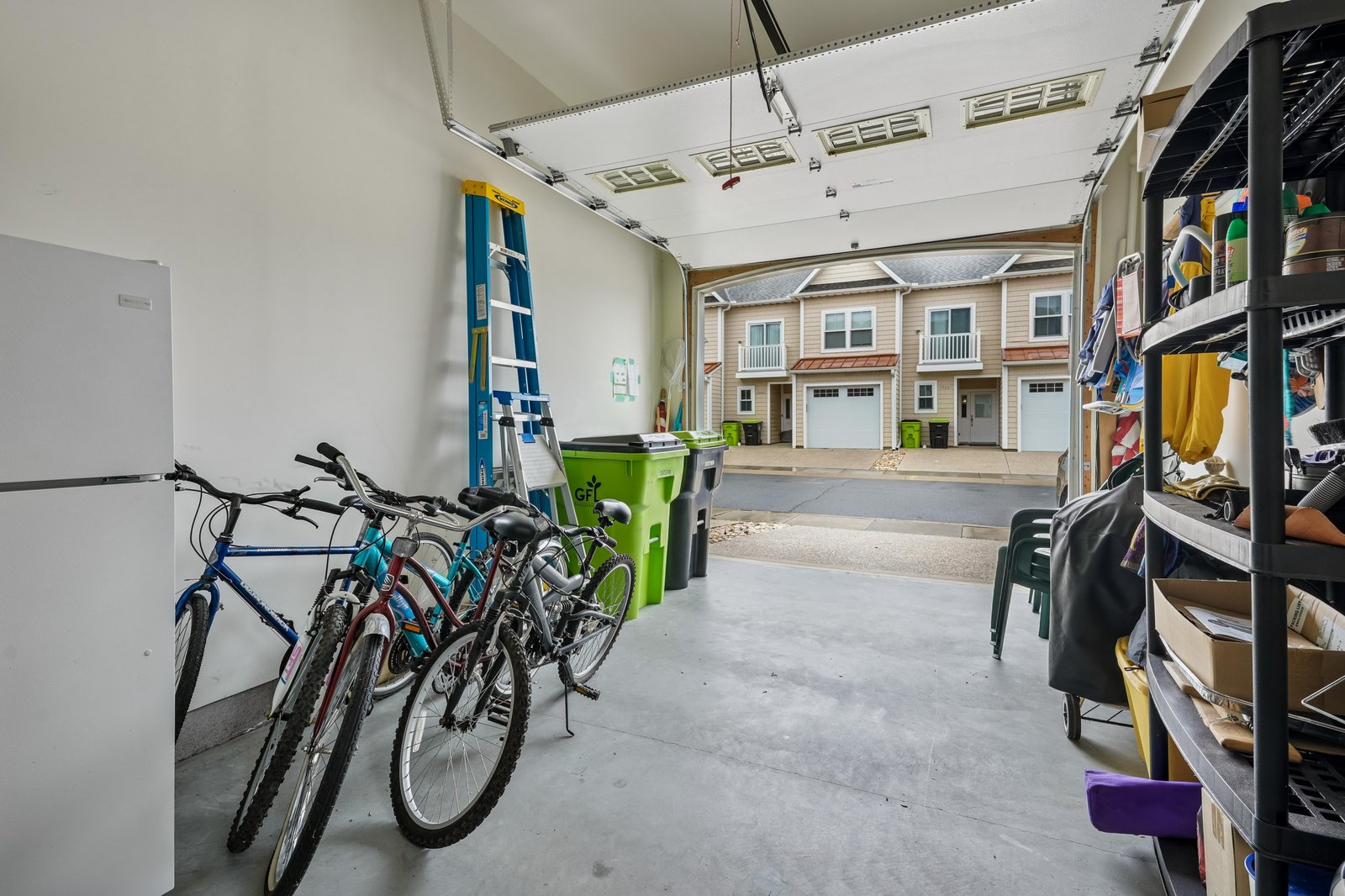 A townhome community framed through an open garage, with convenient bike storage and organized shelving. Nestled in a quiet residential neighborhood, perfect for easy suburban living.