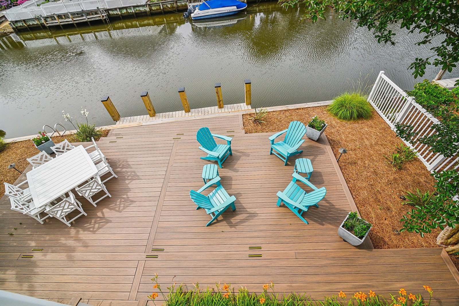 An expansive waterfront deck with cheerful turquoise chairs overlooks private boat dockage along a peaceful canal—perfect for morning coffee or sunset gatherings by the water.