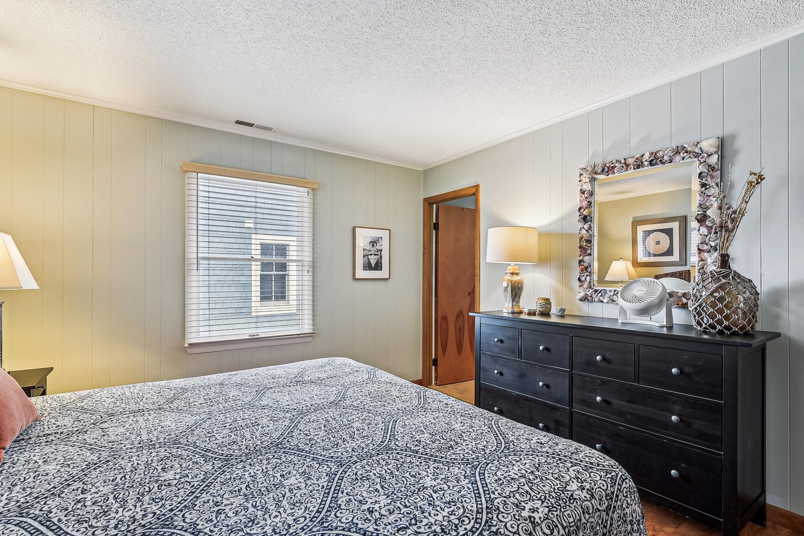 Sink into a cozy bedroom where soft paneling and thoughtful decor create a peaceful retreat. Your personal dresser and charming coastal touches set the stage for a restful stay.