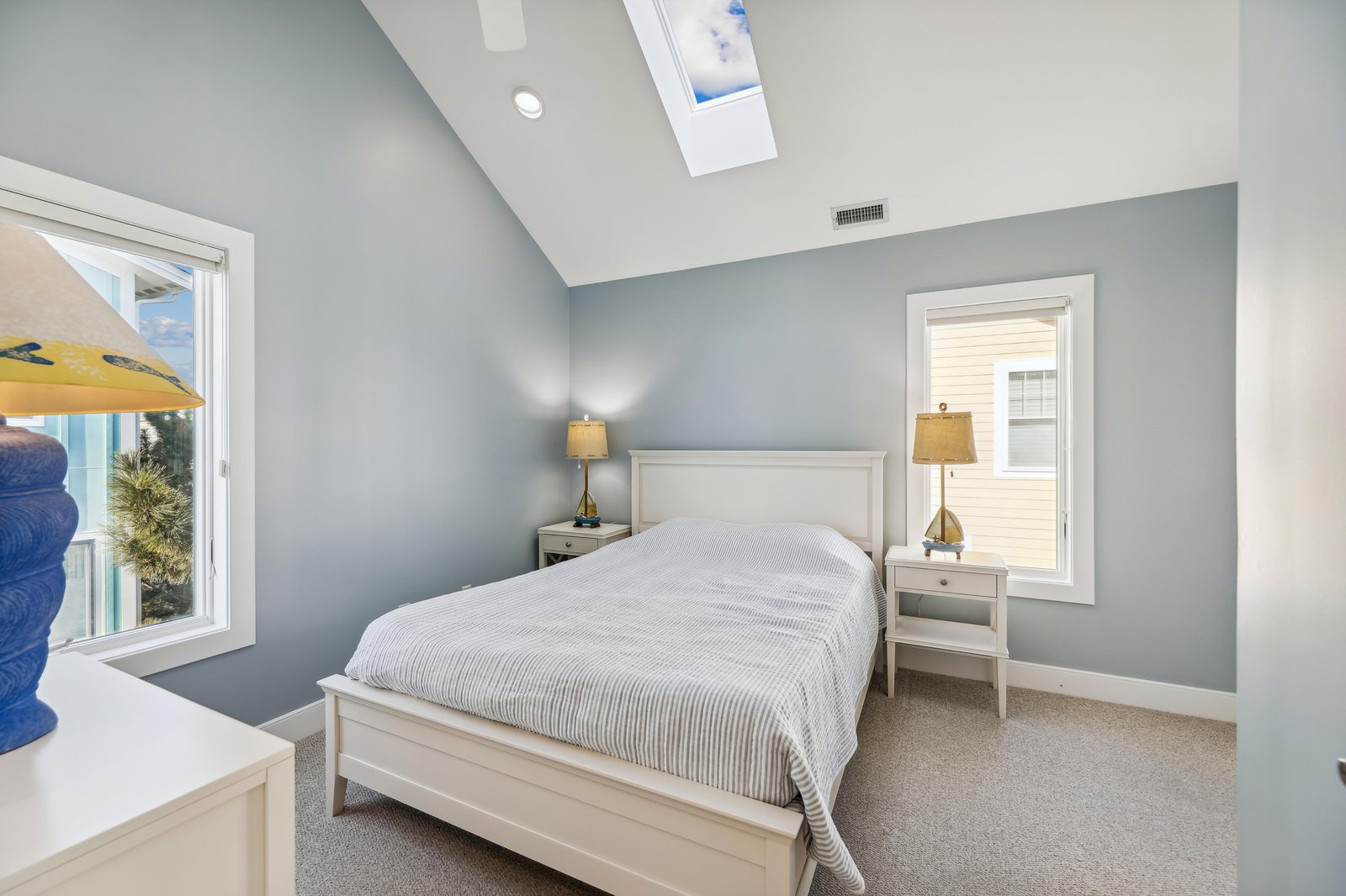 Drift off under the skylight in your serene bedroom, where soothing blue-gray walls and a cozy striped duvet invite deep relaxation after your beachside adventures.