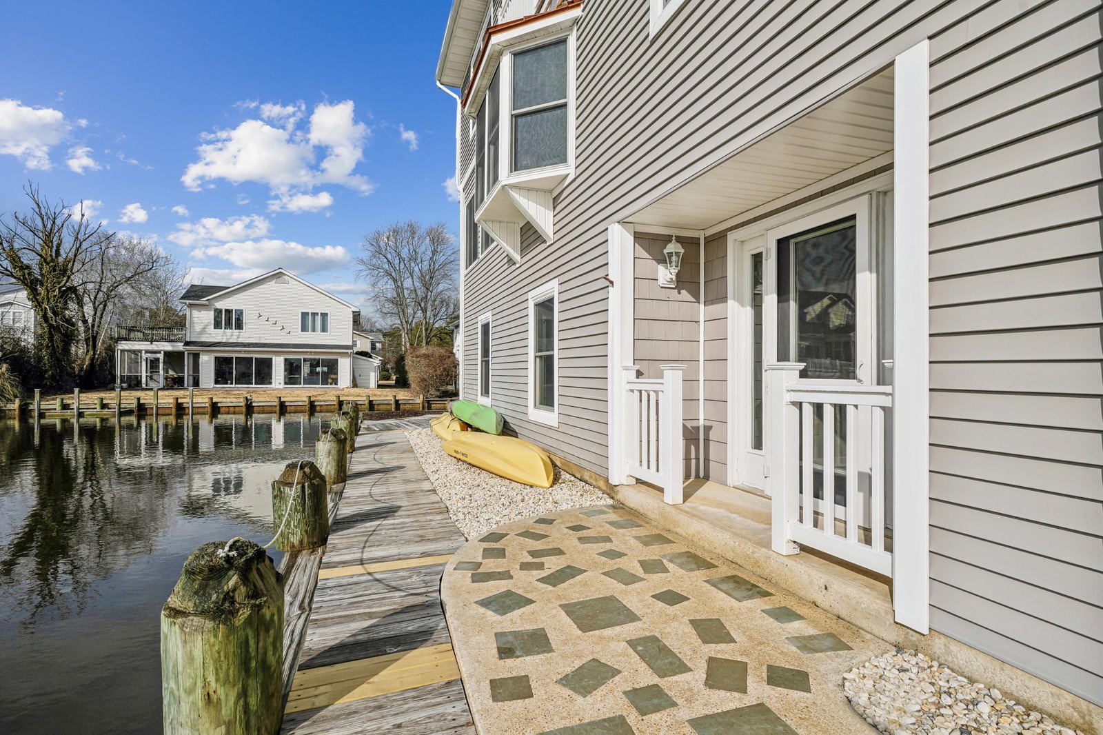 Waterfront property with private dock and scenic canal access, featuring covered entry porch, outdoor patio space, and kayaks for exploring the serene neighborhood waterways.