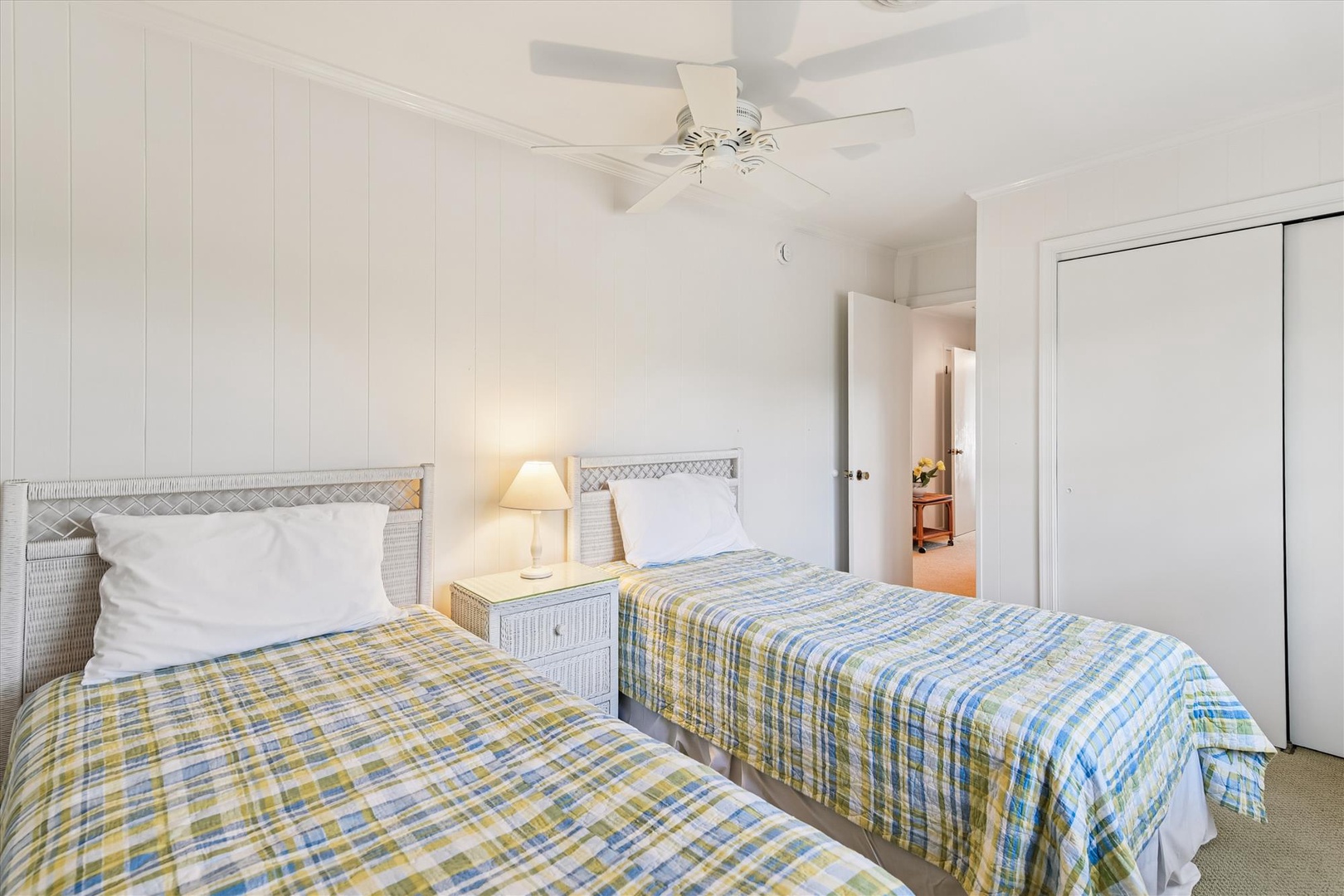 Your bright twin bedroom features cheerful plaid bedding and wicker headboards, with a gentle ceiling fan creating the perfect coastal retreat.