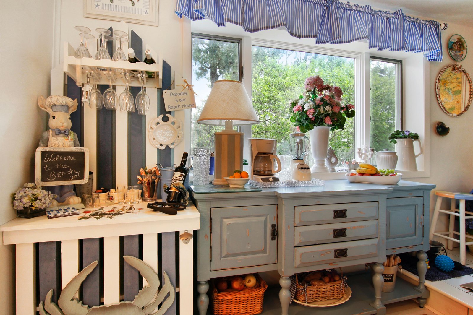 Sink into this charming coastal-inspired space, where natural light filters through windows framing lush greenery. Fresh flowers, warm wood tones, and vintage cottage touches create your perfect retreat.