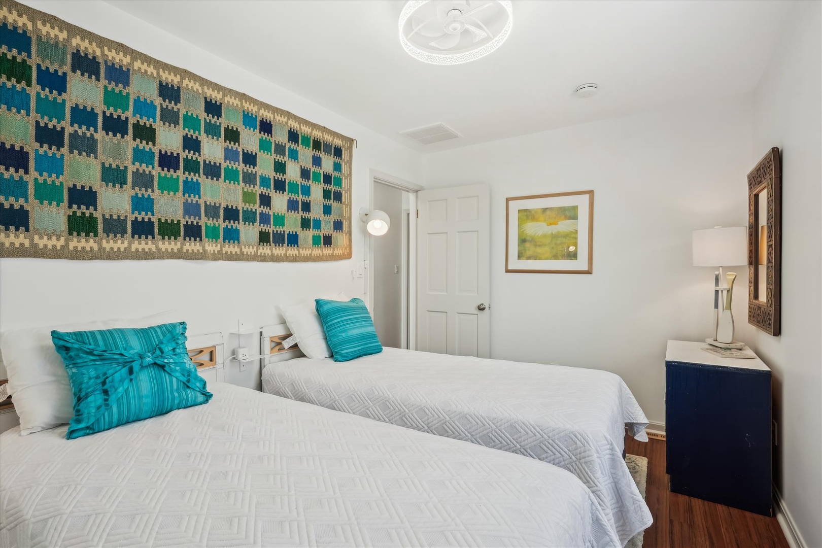 Your bright bedroom features two plush beds with crisp white linens and vibrant turquoise accents that bring calm coastal energy. Art and personal touches create a welcoming retreat.