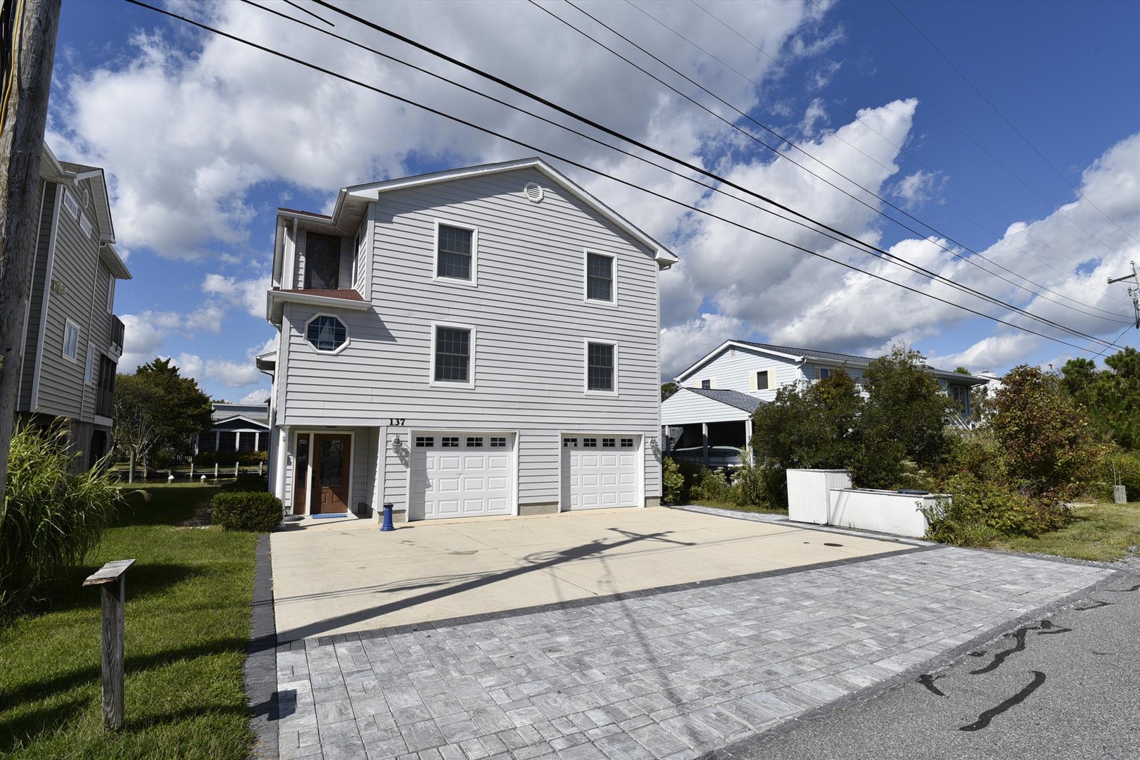 A modern three-story vacation home located in a quiet residential neighborhood, featuring a two-car garage and spacious driveway with ample parking for guests.