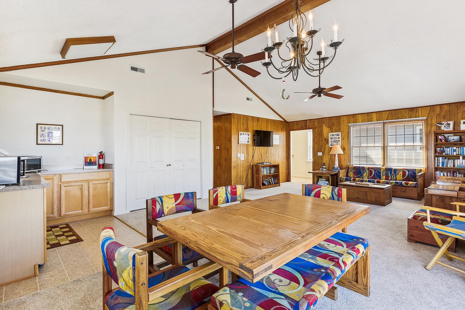 Spacious open-concept living area with vaulted ceilings, rustic wood accents, and colorful seating perfect for your gathering. Bright natural light fills the room through large windows.