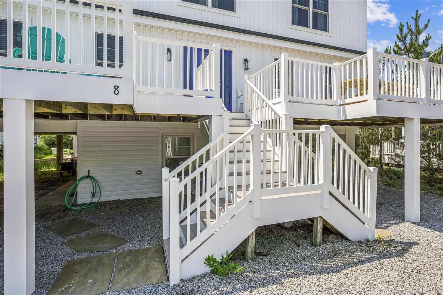 Elevated coastal property with white railings and deck access above garage parking. The bright exterior and multi-level design offer convenient beach-style living just steps from the surf.