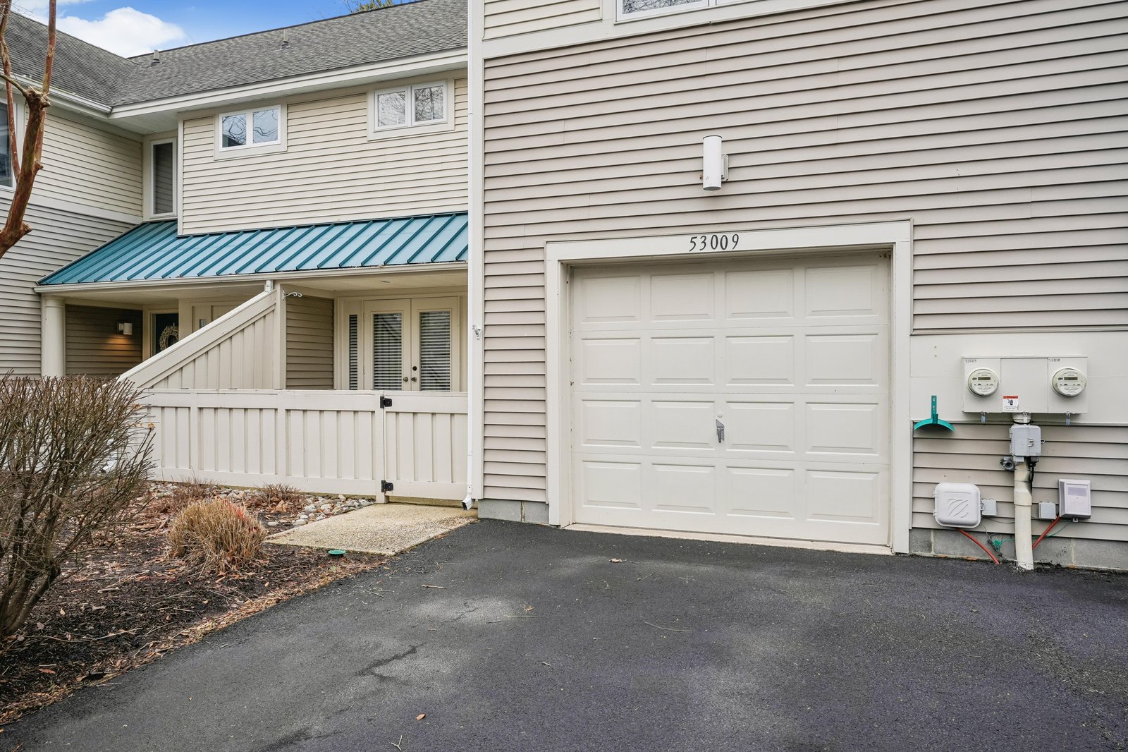 Property entrance and garage located at 53009. The home features beige vinyl siding with a teal metal awning over the front entrance and convenient parking access.