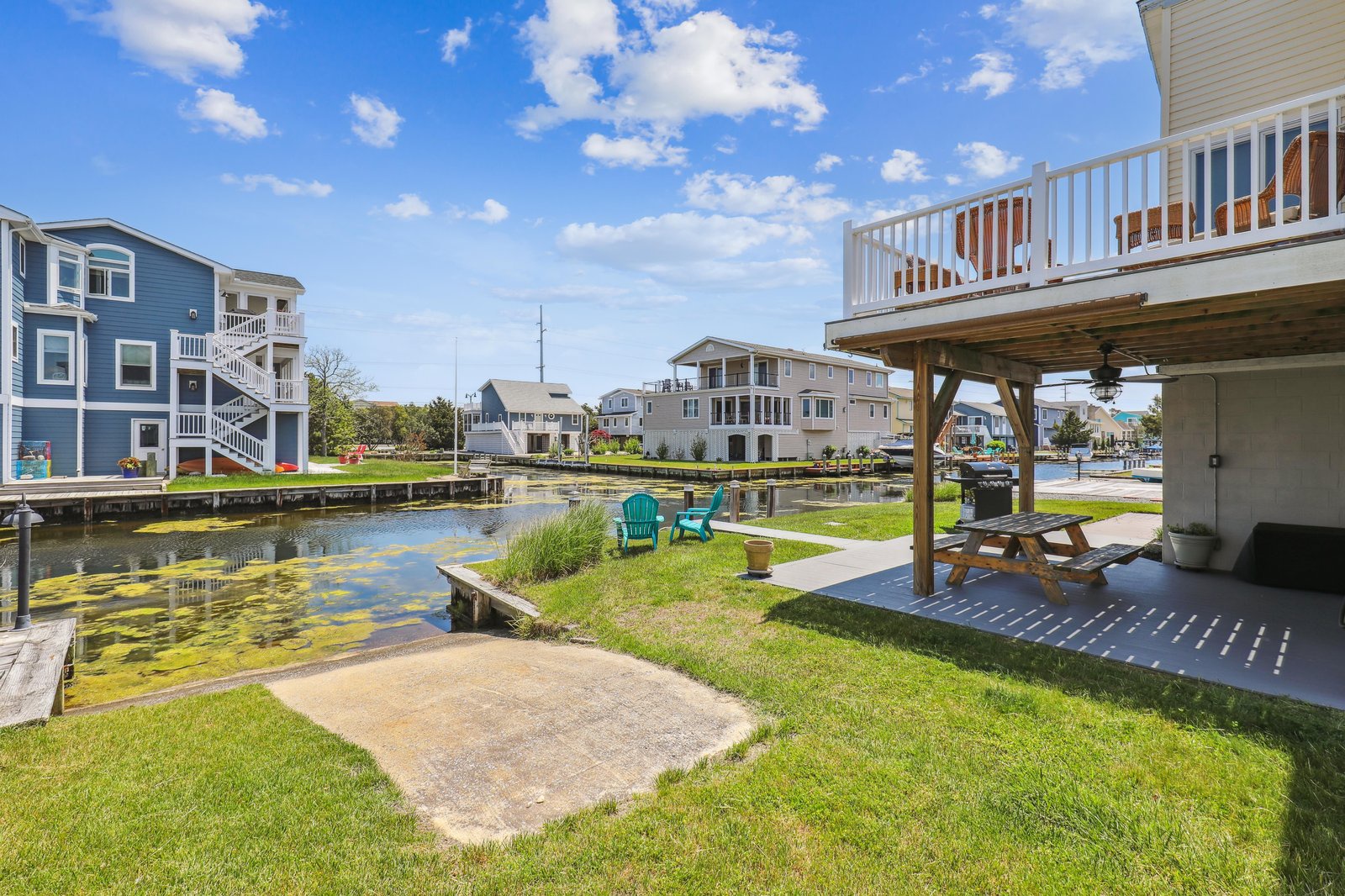 Waterfront backyard with direct canal access, covered deck, private dock, and colorful Adirondack chairs overlooking a tranquil neighborhood channel—perfect for morning coffee or evening gatherings.