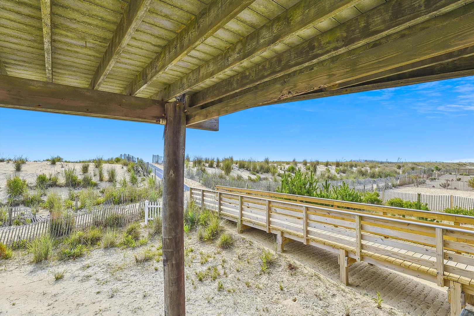This property offers direct access to the beach via a scenic sandy path with dune grasses and clear blue skies. The covered seating area provides shade on sunny days.