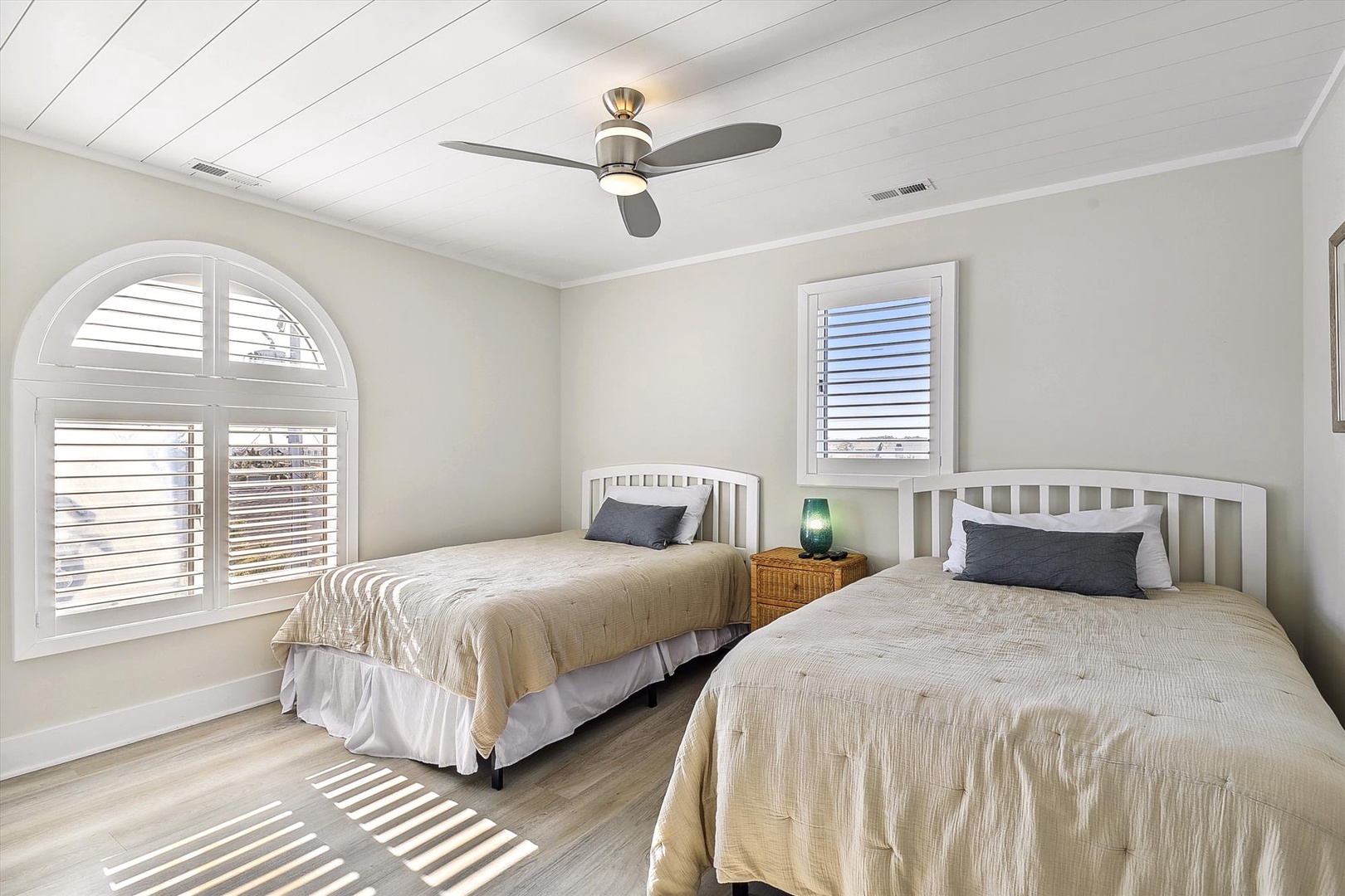 Rest easy in your serene coastal bedroom with two comfortable beds and gentle natural light filtering through plantation shutters, keeping you cool and relaxed.