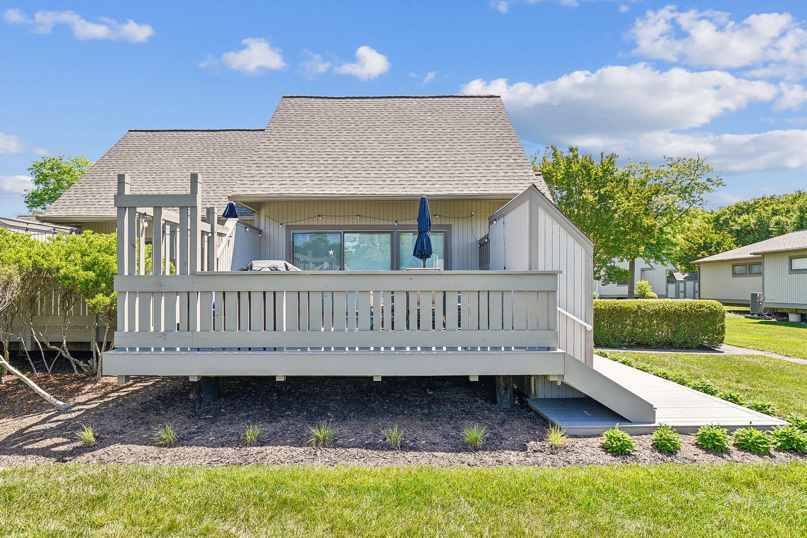 Modern beach house with spacious deck and coastal design, surrounded by lush landscaping in a peaceful residential setting.