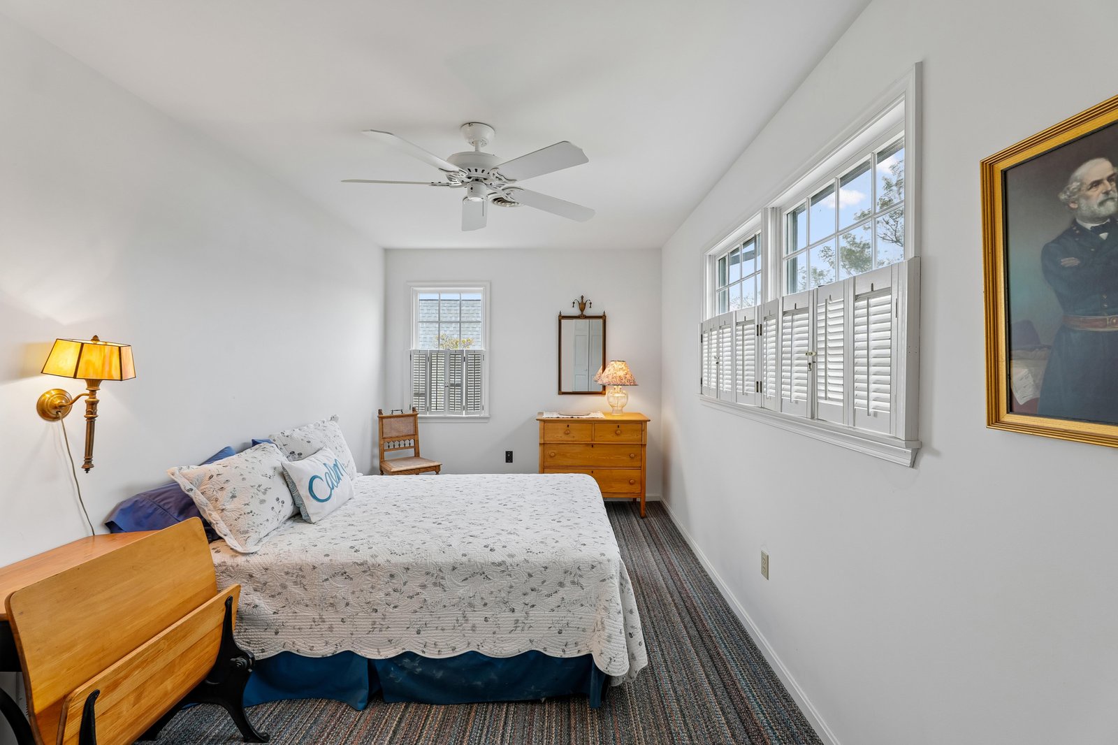 Step into your private retreat with a cozy bed, gentle ceiling fan, and bright natural light filtering through the plantation shutters.
