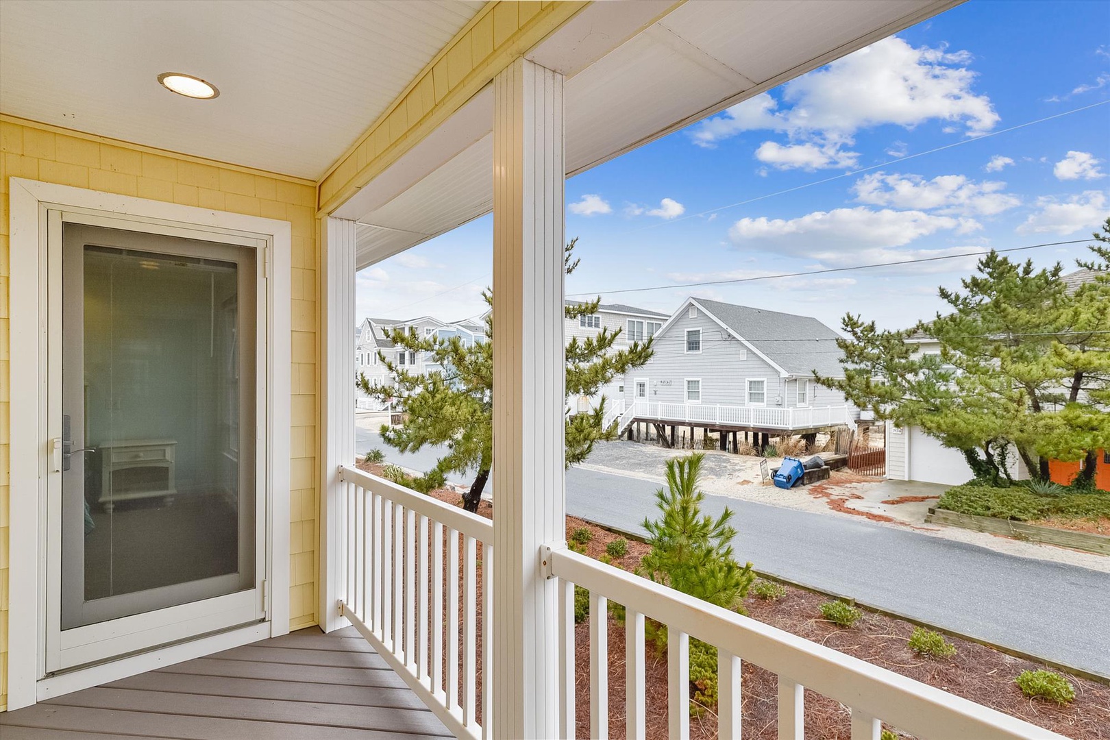 A covered balcony with white railings and pine views, located in a coastal residential neighborhood with nearby beach properties.