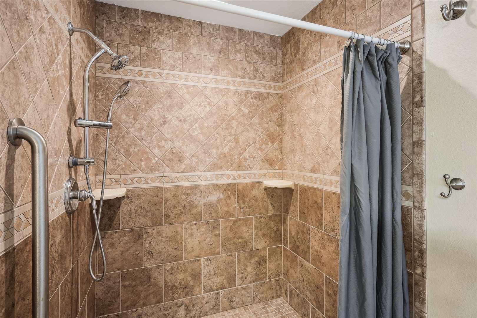 Your private shower features elegant tile work and a convenient handheld showerhead for a comfortable, refreshing experience after each day of exploring.