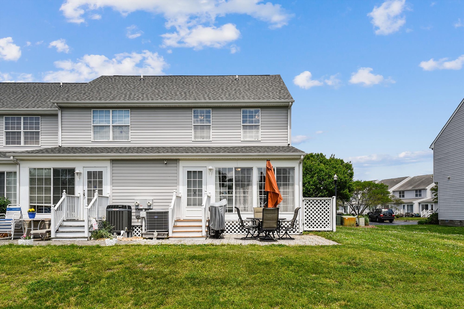 Spacious two-story vacation home with private backyard patio seating, perfect for relaxing under sunny skies in a quiet residential neighborhood setting.