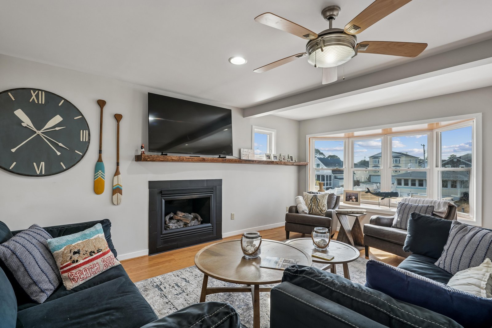 Cozy up by the fireplace in this inviting living room, where soft seating, warm wood tones, and a stylish ceiling fan create the perfect retreat after your coastal adventures.
