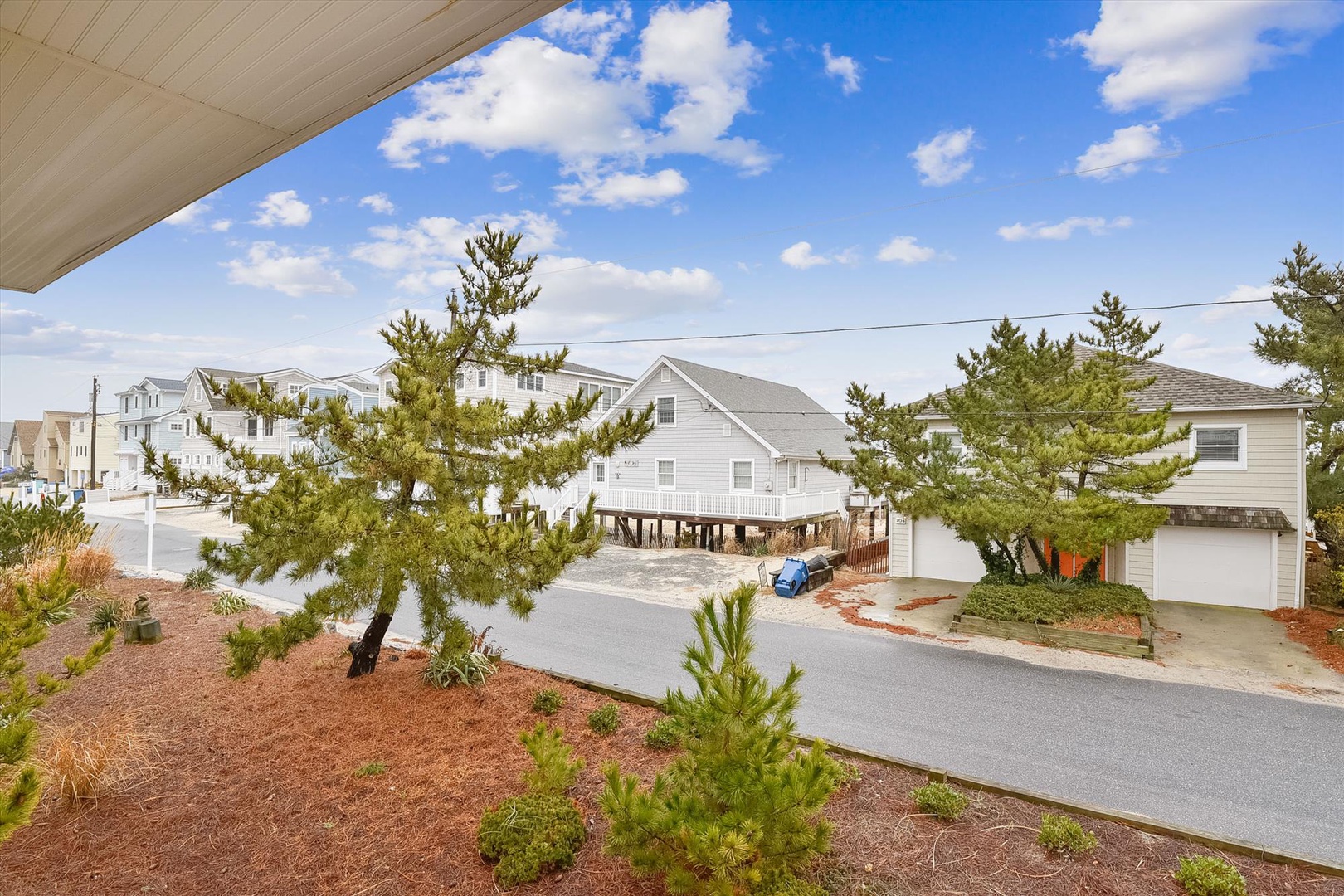Coastal residential neighborhood with elevated beach homes, mature landscaping, and ample parking in a peaceful setting under bright blue skies.