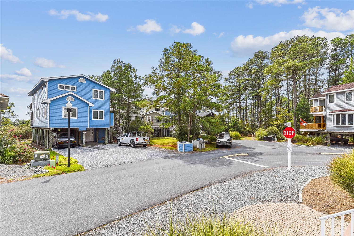 A peaceful coastal neighborhood greets visitors with a vibrant blue beach house, shaded streets, and easy parking—the perfect base for your seaside escape.